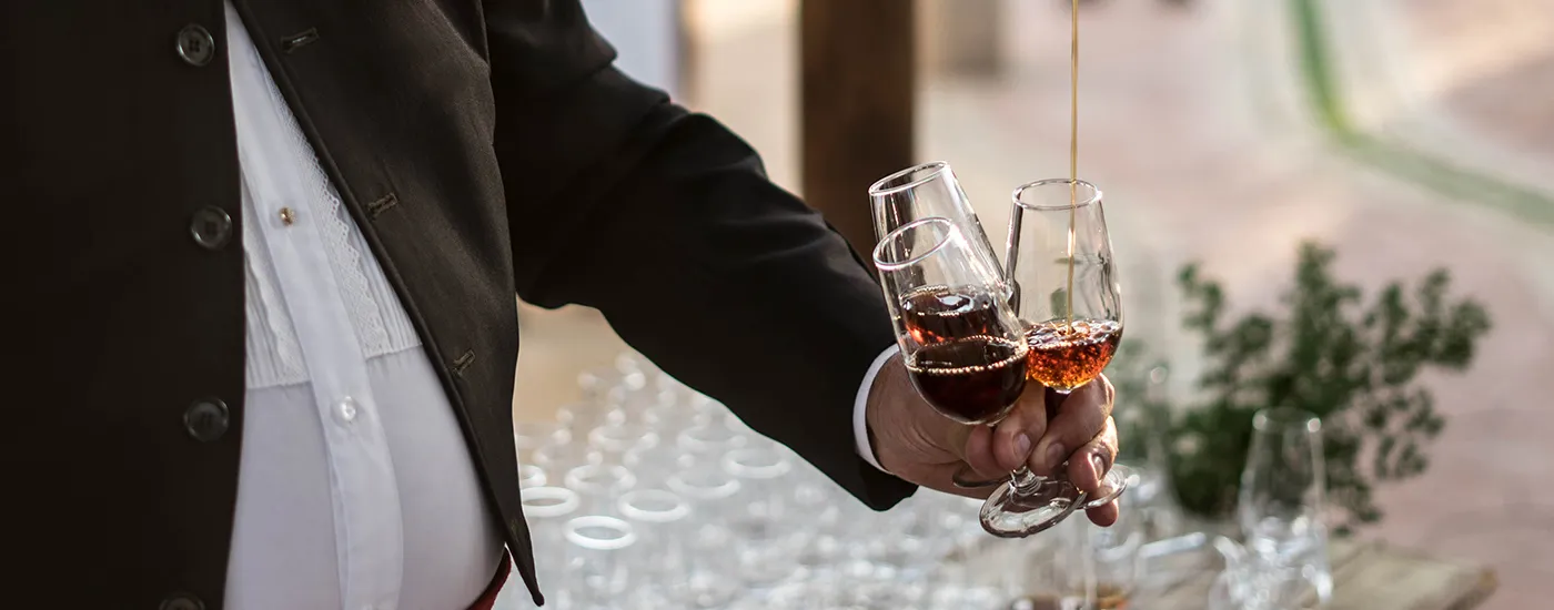 Mano con dos copas de vino tinto en una celebraci&oacute;n al aire libre