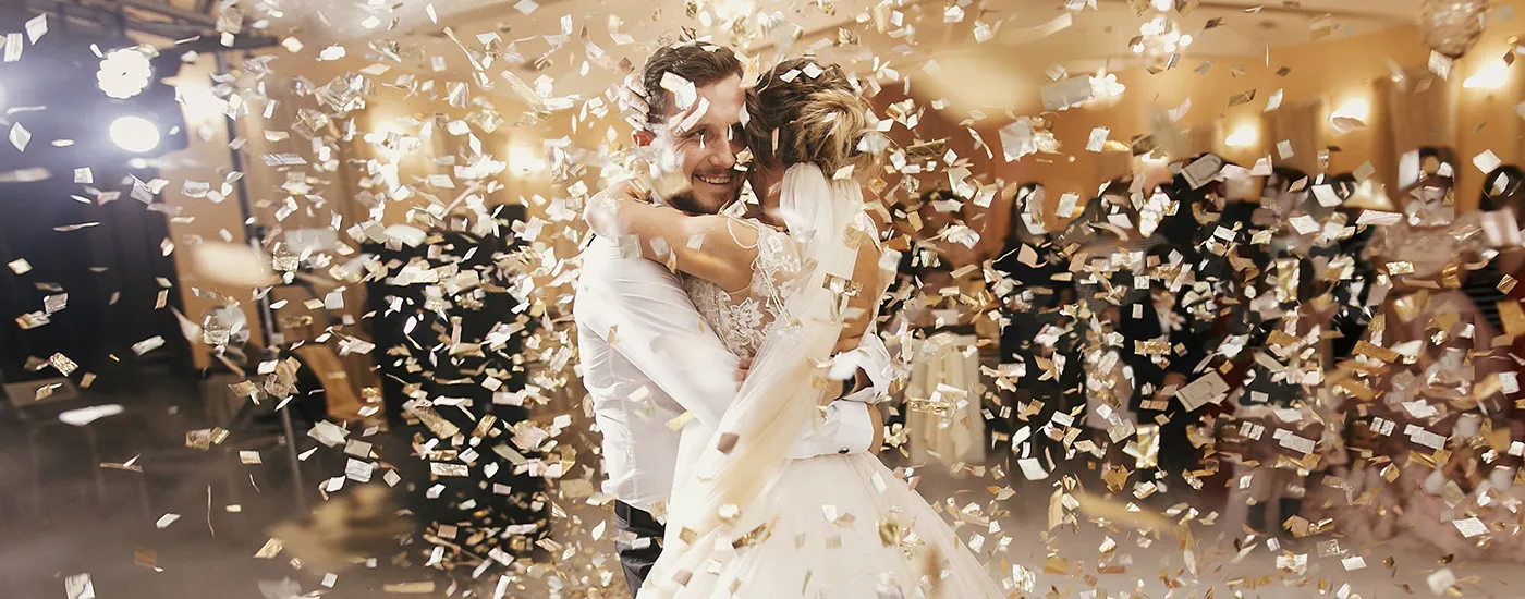 Pareja de novios sonriendo con confeti dorado en el aire en una celebraci&oacute;n.