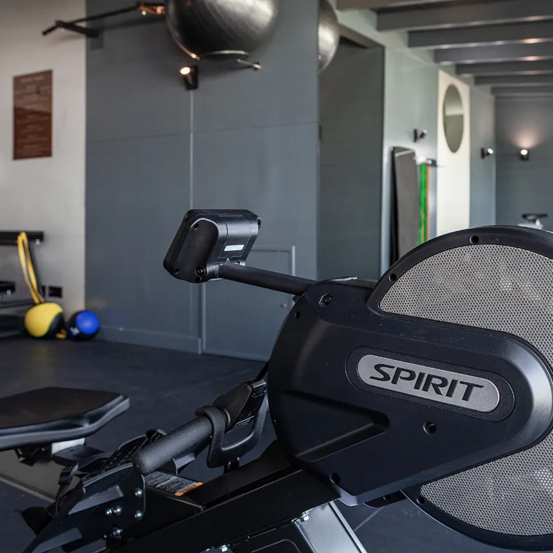 Cinta de correr negra &ldquo;SPIRIT&rdquo; en gimnasio, con equipo y pesas al fondo.