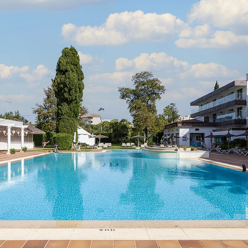 Piscina azul con edificios y &aacute;rboles bajo un cielo con nubes.