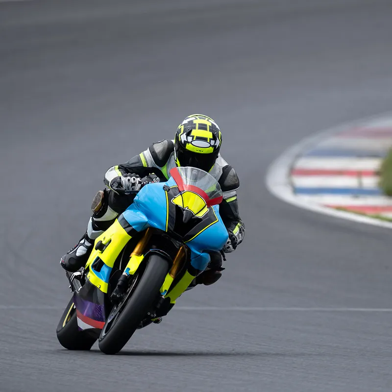 Piloto de moto de carreras con casco amarillo y azul inclin&aacute;ndose en la pista