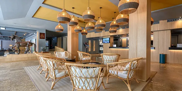 Sala de hotel con mesas de mimbre, sillas y l&aacute;mparas colgantes.