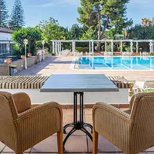 Patio con piscina y mesas al aire libre, rodeado de jardines y &aacute;rboles.