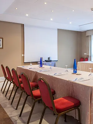 Sala de reuniones con mesas rectangulares, sillas rojas y proyector