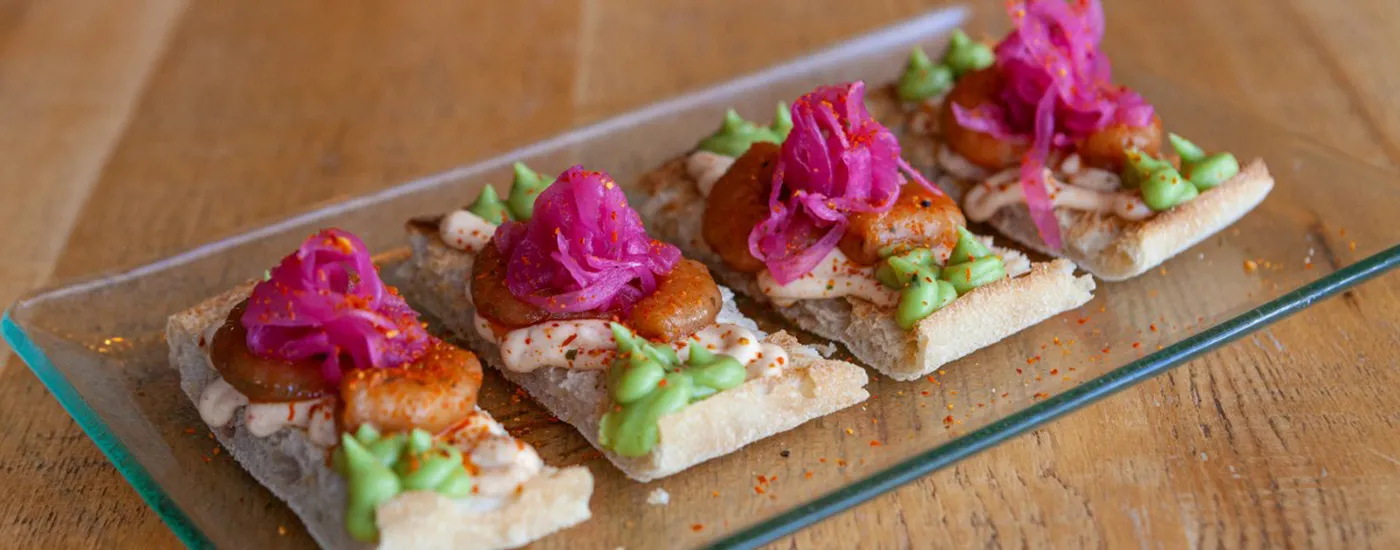Tostas con pollo, cebolla morada encurtida y verduras sobre bandeja de vidrio