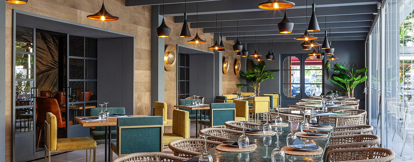 Comedor moderno con mesas, sillas tejidas, copas y l&aacute;mparas colgantes en interior