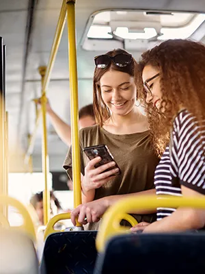 Dos mujeres charlando en el bus y una mira el m&oacute;vil.