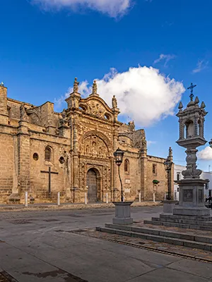 Fachada de una catedral de piedra con cruces, cielo azul y nubes.