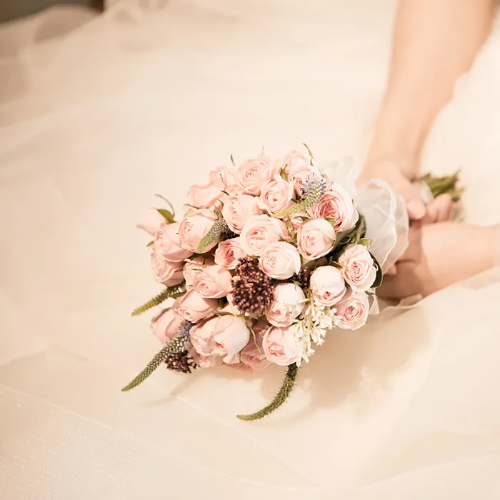 Ramo de rosas rosadas en manos con vestido de novia, en primer plano.