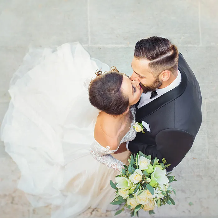 Novios bes&aacute;ndose en boda, con ramo de flores blancas y verdes.