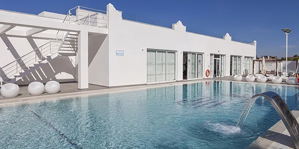 Piscina exterior con jacuzzi y edificio blanco moderno junto al mar