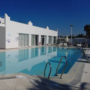 Piscina azul con zona de terraza y edificio blanco bajo cielo despejado.