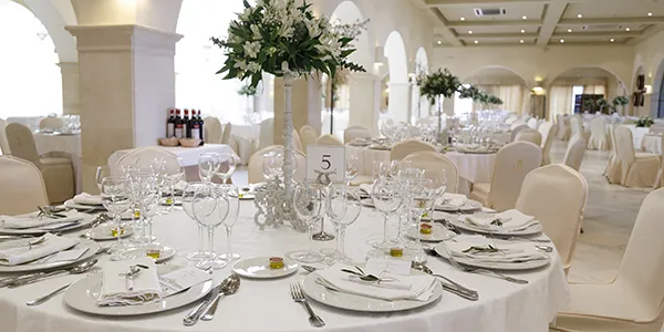 Mesa decorada de banquete con copas y centros florales en sal&oacute;n blanco