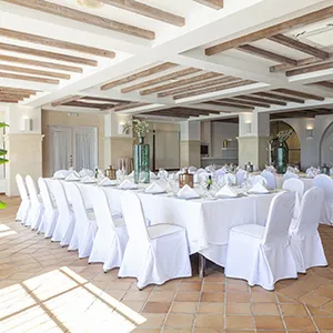 Sal&oacute;n de banquetes con mesas y sillas blancas decoradas.