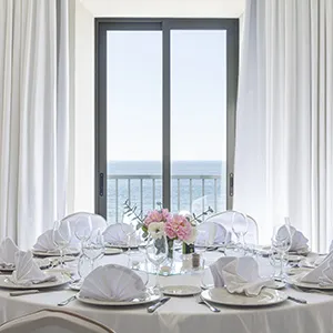 Mesa puesta frente a ventana con vista al mar y flores rosadas