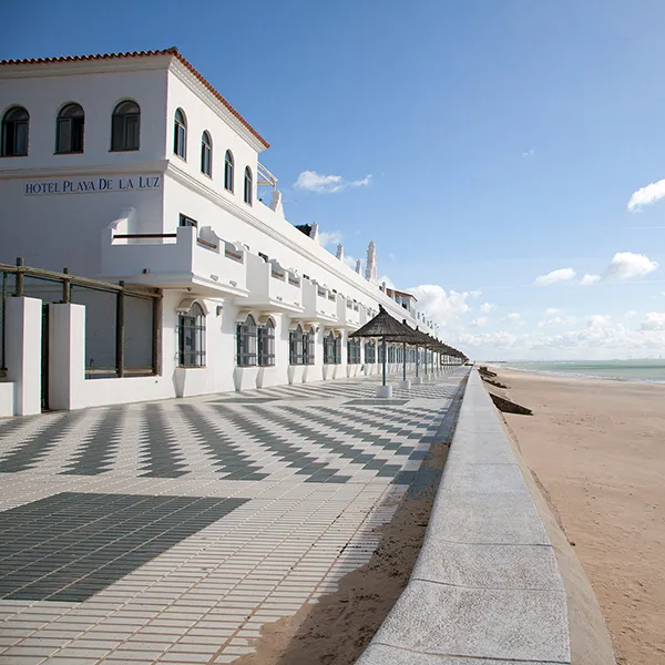 Hotel Playa de la Luz junto al mar, con pasillo y fachada blanca.