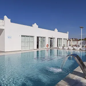 Piscina azul con edificio blanco y cielo despejado al atardecer.
