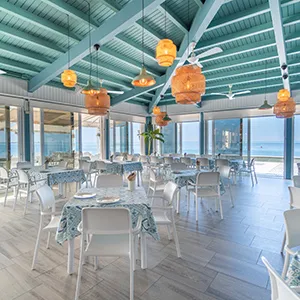 Comedor luminoso con mesas y sillas blancas bajo l&aacute;mparas colgantes.