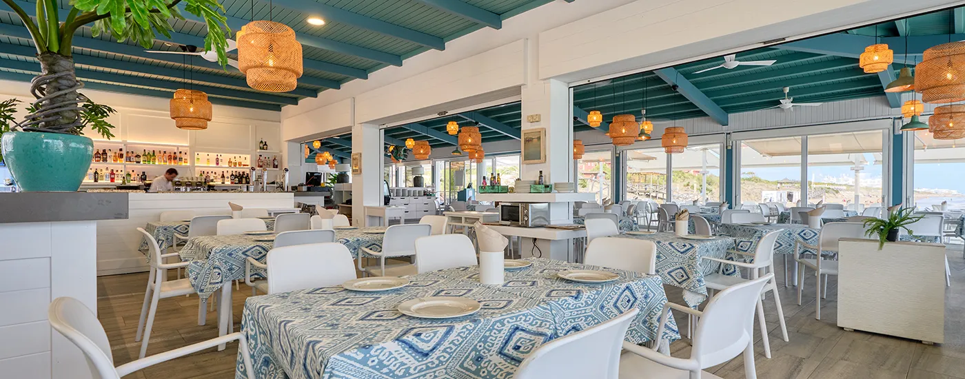 Interior de restaurante con mesas, sillas blancas y l&aacute;mparas colgantes de mimbre