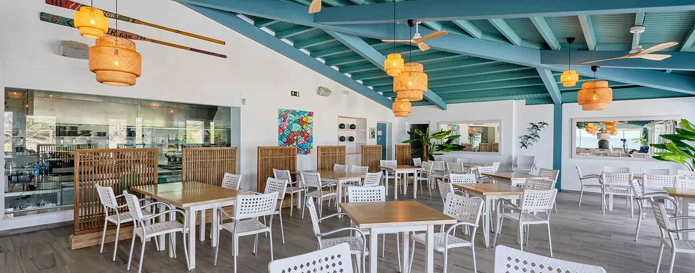 Terraza interior con mesas y sillas, l&aacute;mparas colgantes y techo de madera.