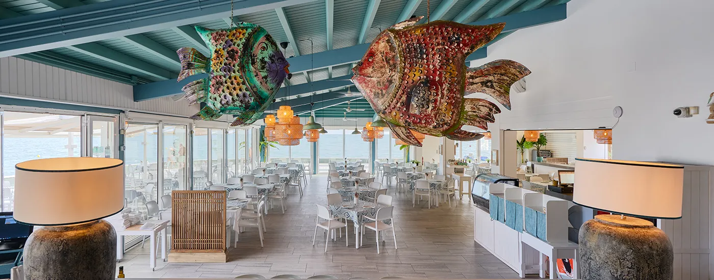 Restaurante interior con l&aacute;mparas de techo y grandes decoraciones de peces colgantes.