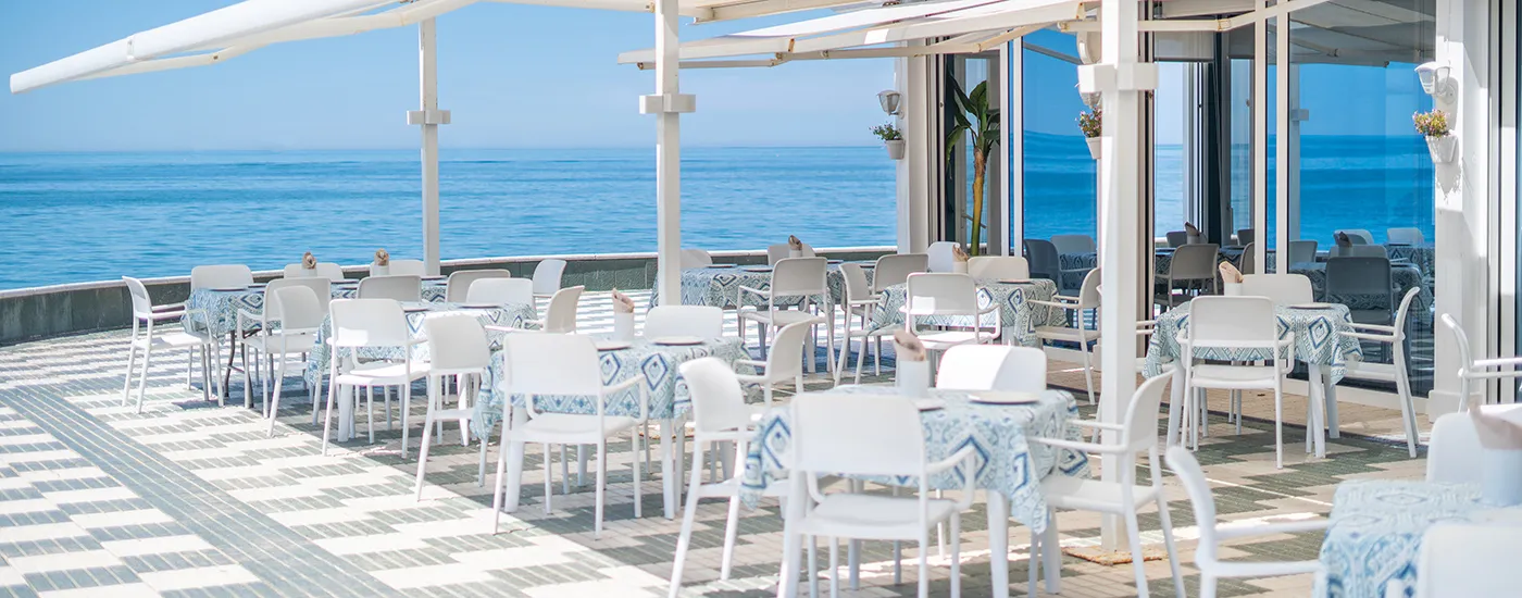 Terraza con mesas y sillas blancas junto al mar, vista azul del oc&eacute;ano.