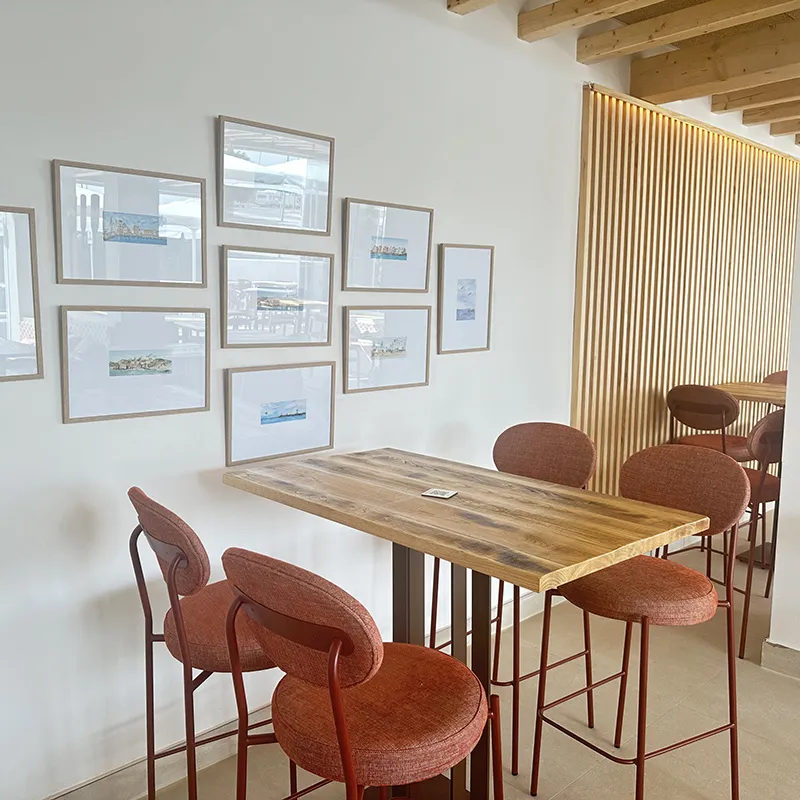 Sala con mesa de madera y sillas frente a panel de lamas de madera y cuadros