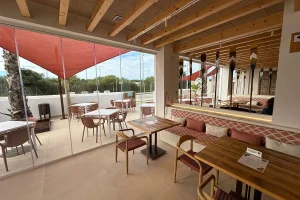 Terraza moderna con mesas, sillas y cortinas rojas, en hotel.