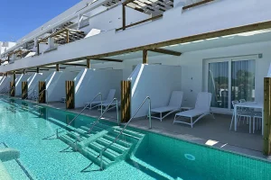 Piscina junto a terraza con tumbonas y escalera en hotel de fachada blanca.