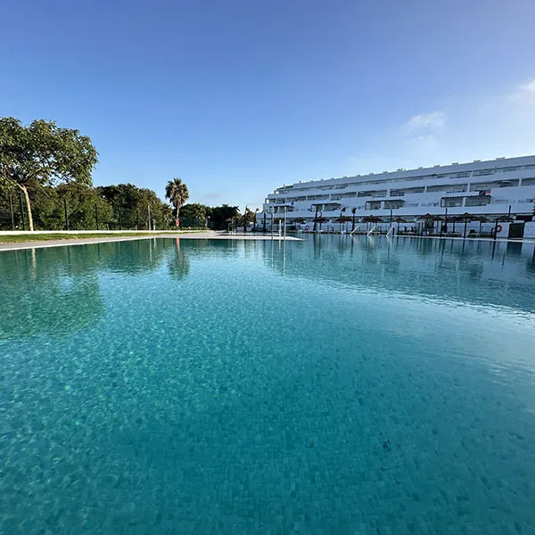 Piscina azul con edificio blanco y palmeras al fondo bajo cielo despejado