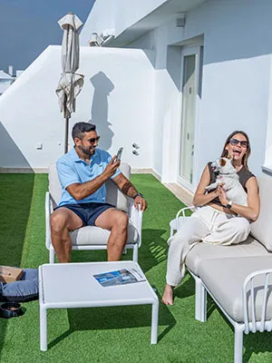 Dos personas relajadas en sillas blancas en un patio con c&eacute;sped.