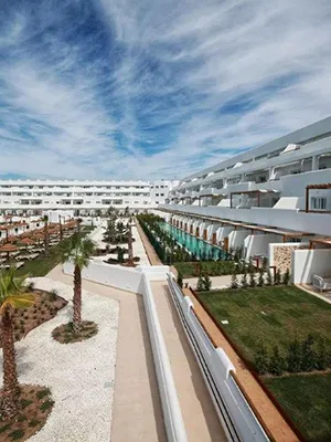 Pasillo con jard&iacute;n y edificios blancos bajo cielo nublado en resort