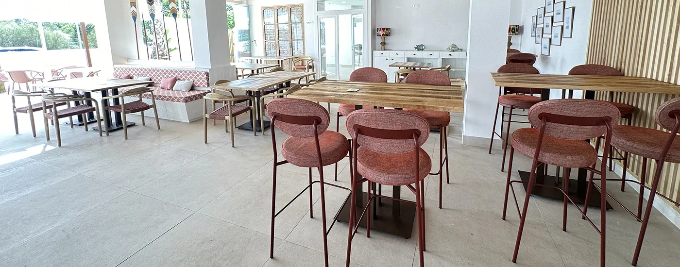 Sal&oacute;n luminoso con mesas y sillas de madera, con decoraci&oacute;n y ventanales.