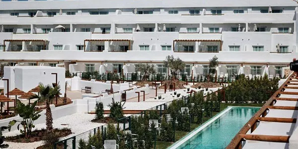 Patio hotelero con piscina, jardines y terrazas blancas al fondo.