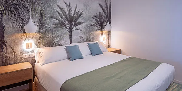 Habitaci&oacute;n de hotel con cama blanca, almohadas azules y paredes tropicales