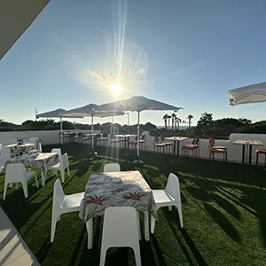 Mesa con sillas blancas en jard&iacute;n, luz del sol y monta&ntilde;a al fondo