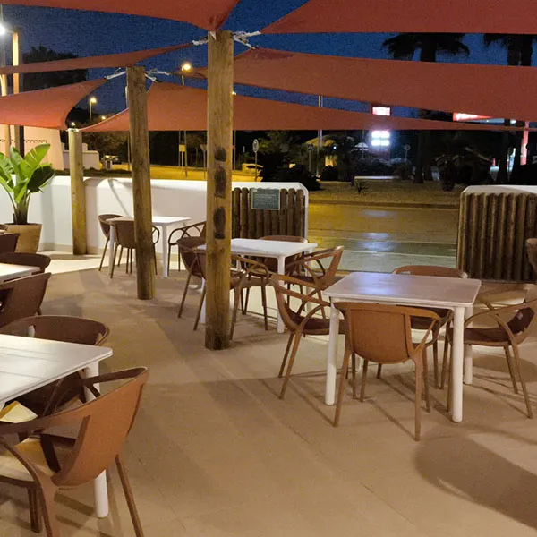 Terraza con sillas y mesas bajo toldos rojos, &aacute;rea exterior al anochecer.
