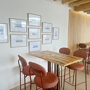 Sala de exposici&oacute;n con mesa de madera y sillas rojas, paredes con p&oacute;sters