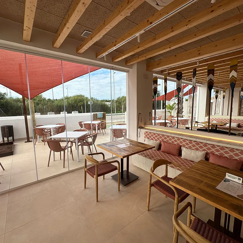 Terraza techada con mesas y sillas, cortinas rojas y pared decorada.