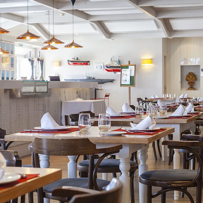 Comedor de restaurante con mesas de madera y copas, manteles blancos y sillas.