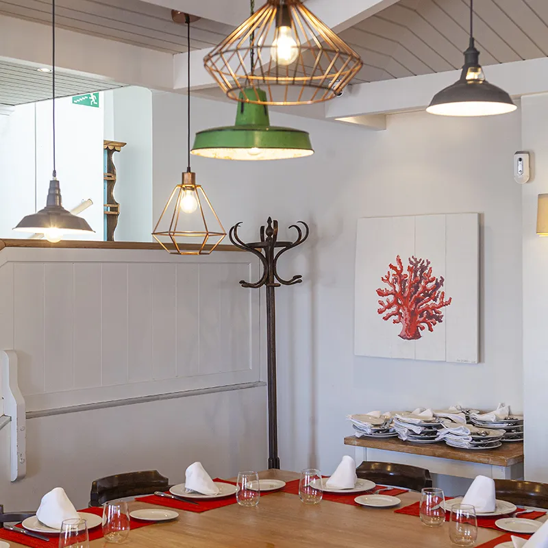 Comedor moderno con mesas y l&aacute;mparas colgantes de estilo industrial y arte coral.