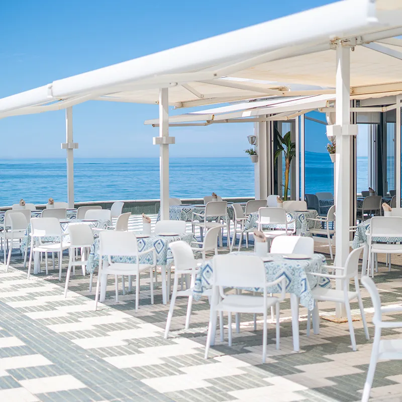 Terraza con sillas blancas bajo toldo, vista al mar azul