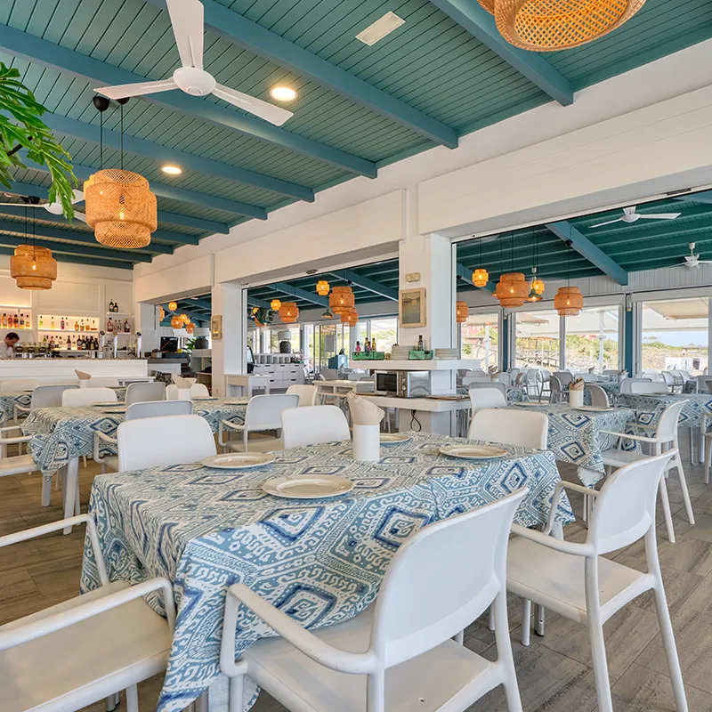 Comedor de hotel con mesas, sillas blancas y candelabros de mimbre bajo techo verde