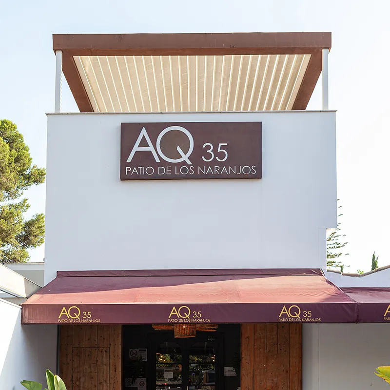 Cartel &ldquo;AQ 35 Patio de los Naranjos&rdquo; en fachada de edificio con marquesina roja