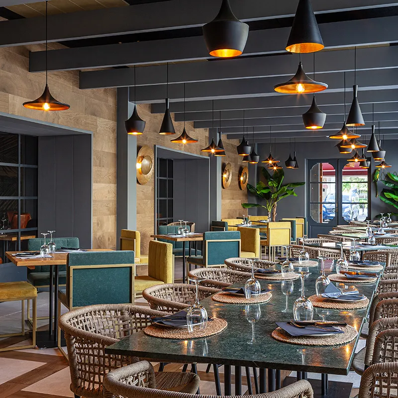 Comedor moderno con mesas servidas y l&aacute;mparas colgantes de luz c&aacute;lida.