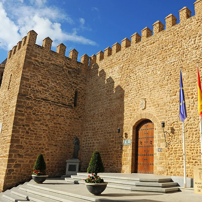 Patio con escalinatas y banderas junto a un castillo de piedra bajo cielo azul