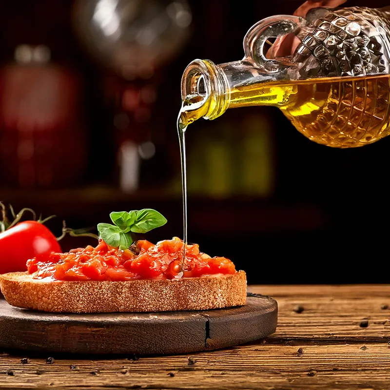 Aceite dorado cayendo sobre tostada con tomate y albahaca, fondo oscuro.