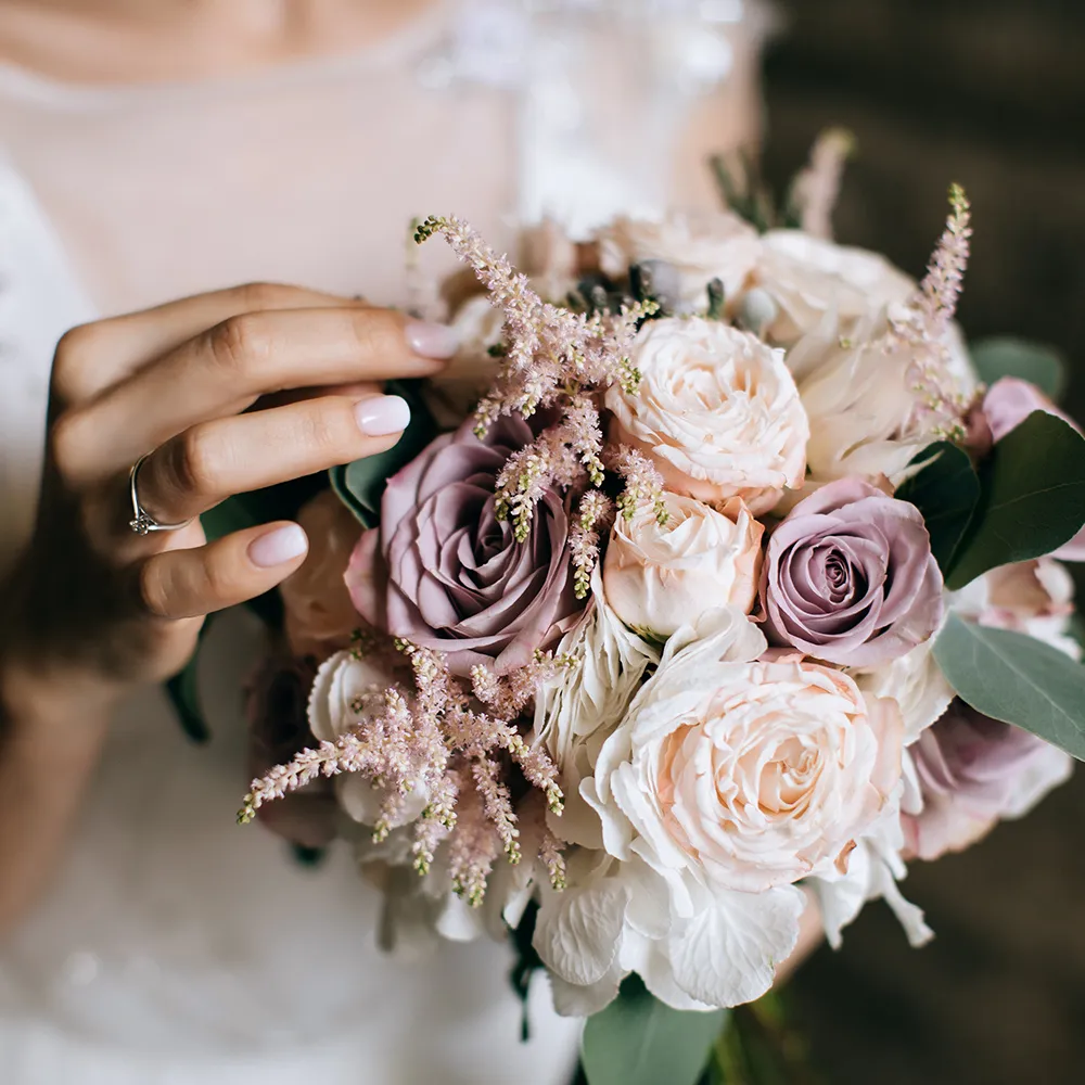 Manos sosteniendo ramo de rosas rosadas y blancas con flores silvestres