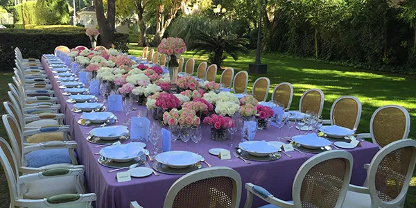 Mesa servida con sillas doradas y centros florales en un jard&iacute;n verde