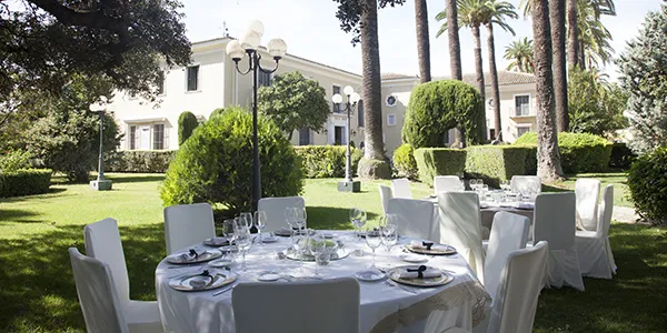 Mesa servida al aire libre en jard&iacute;n con sillas y vajilla, hotel.